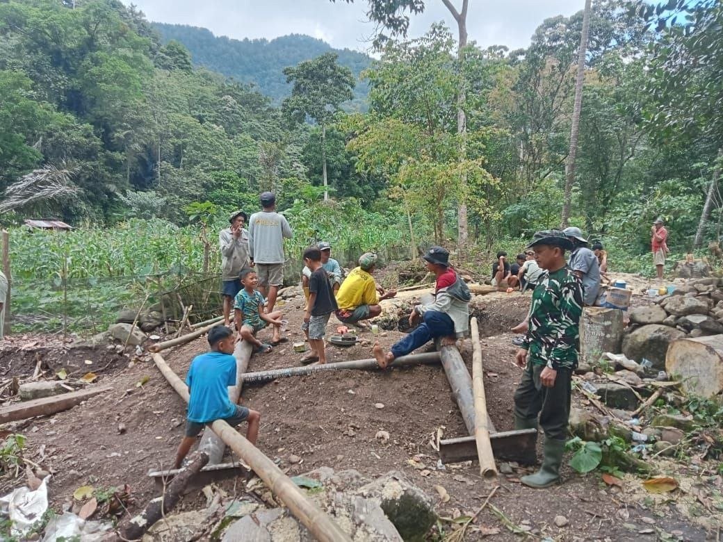 Personel Satgas Bersama Warga Bahu-membahu Memikul Material Besi di Jalur Pembangunan Jembatan Gantung Bone